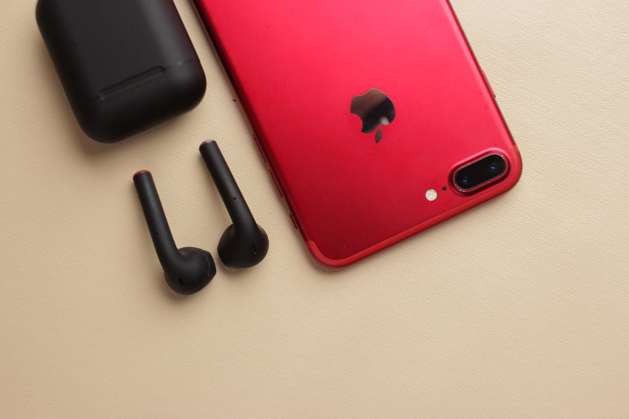 services-03 Close-up of a sleek red smartphone with black wireless earbuds and charging case on a beige surface.